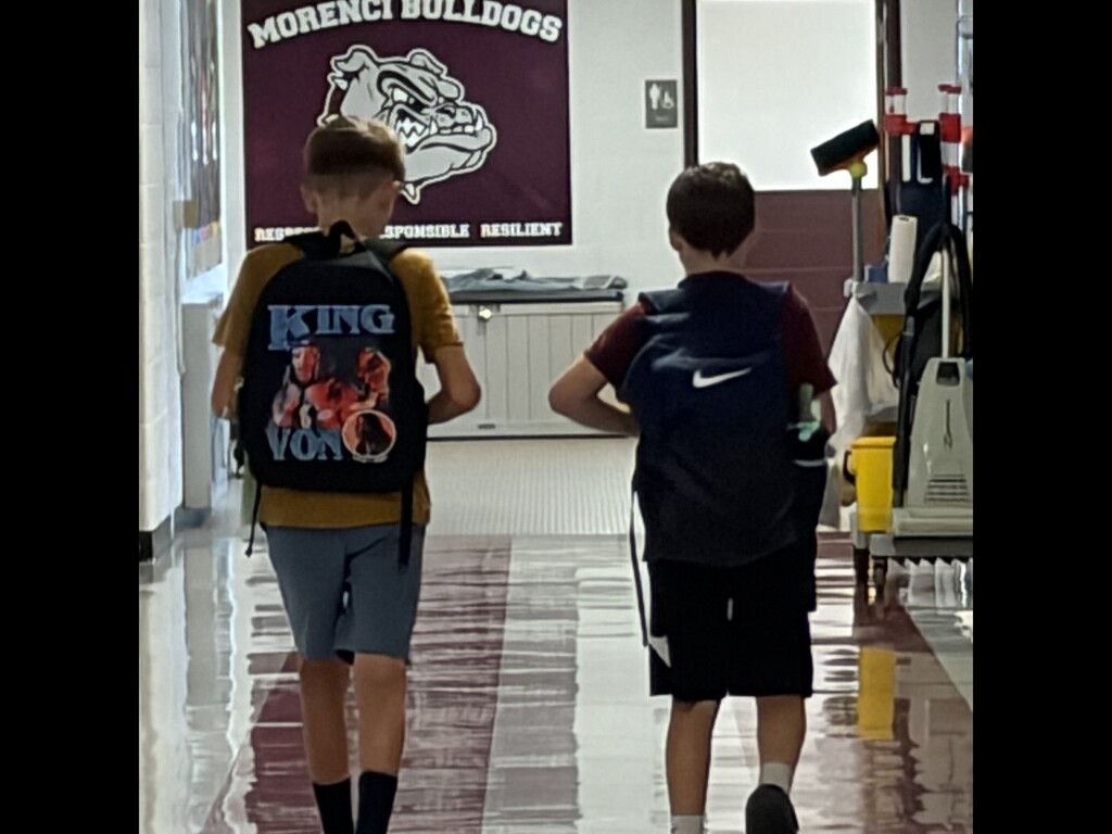 picture of two students walking down the hallway with their backpacks.