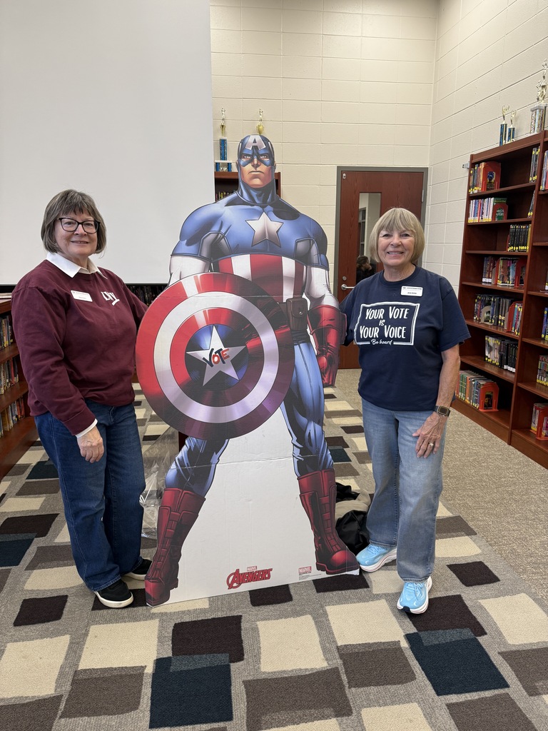two women posting next to super hero