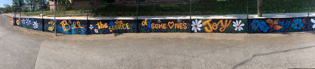 Colorful mural with flowers and bees reads “Be the source of someone’s joy.”