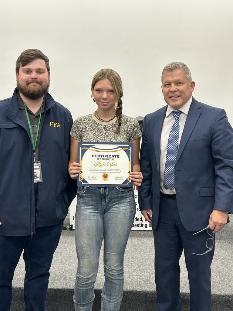 Student honored at board meeting holding FFA certificate with two staff.