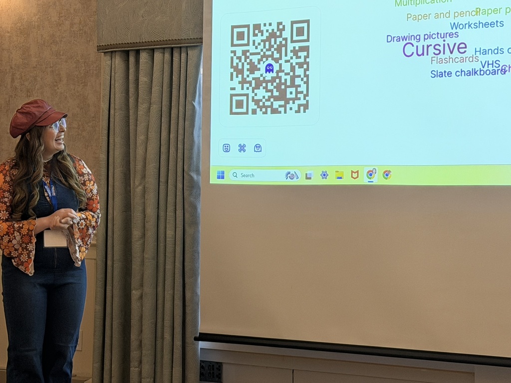 Presenter smiles while showing a slide with a QR code and word cloud.