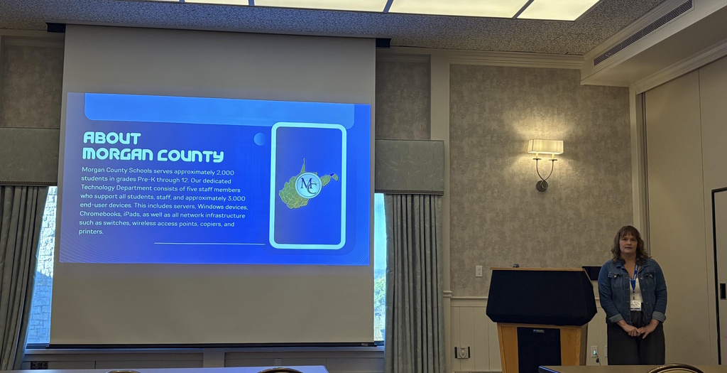 Presenter stands beside a slide titled “About Morgan County Schools.”