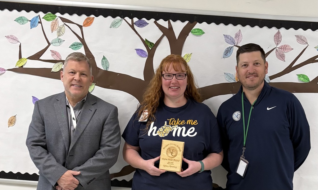 Three people standing in front of a paper tree display holding an award.