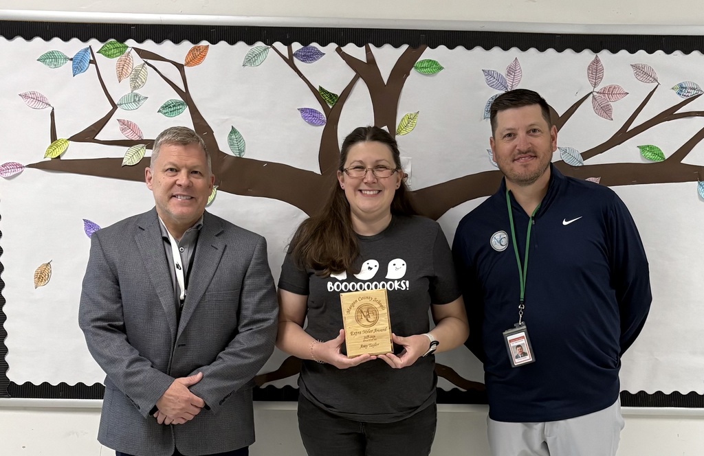 Three people standing in front of a paper tree display holding an award.