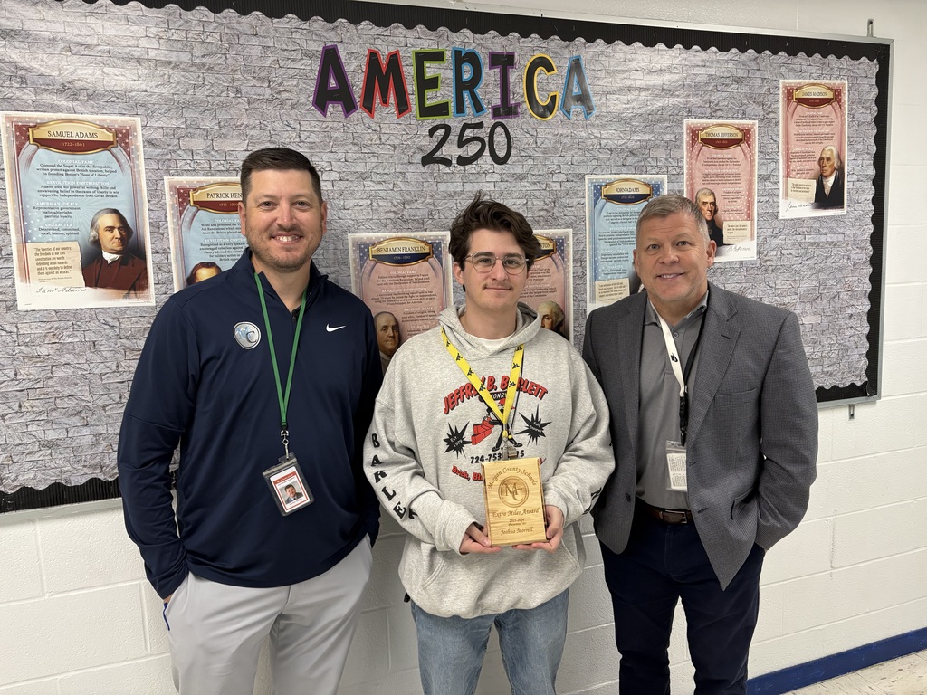 Three people standing in front of a paper tree display holding an award.