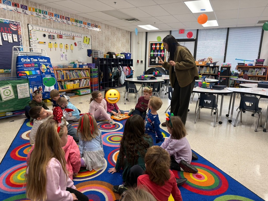 Teacher is giving directions to students sitting on the rug. 