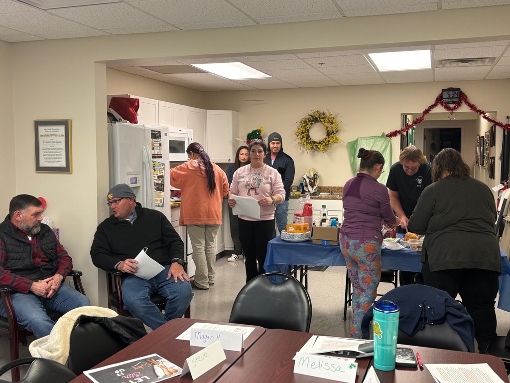 7 parents are chopping up food and cooking on the stovetop. The Food Lion store manager and his director are chatting nearby.