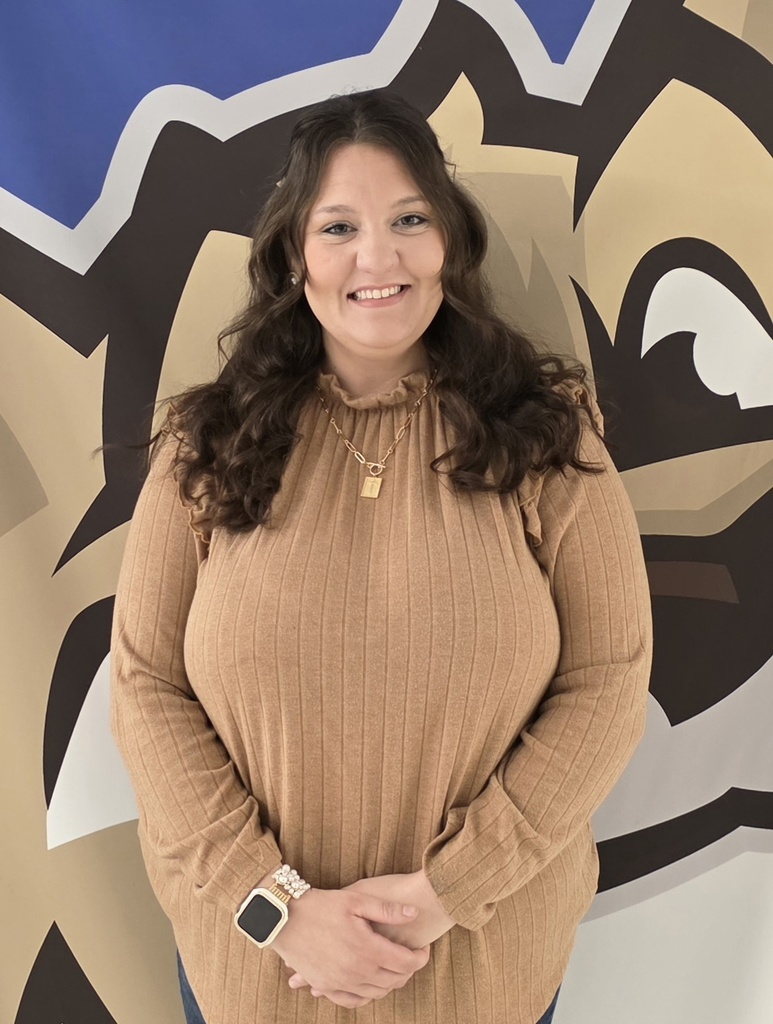 Smiling woman in tan sweater standing before school mural