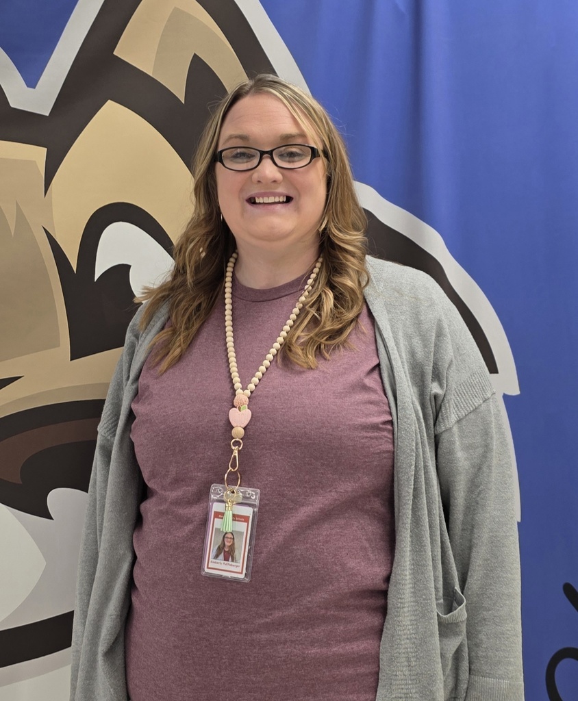 Smiling woman with glasses wearing ID badge at school mural