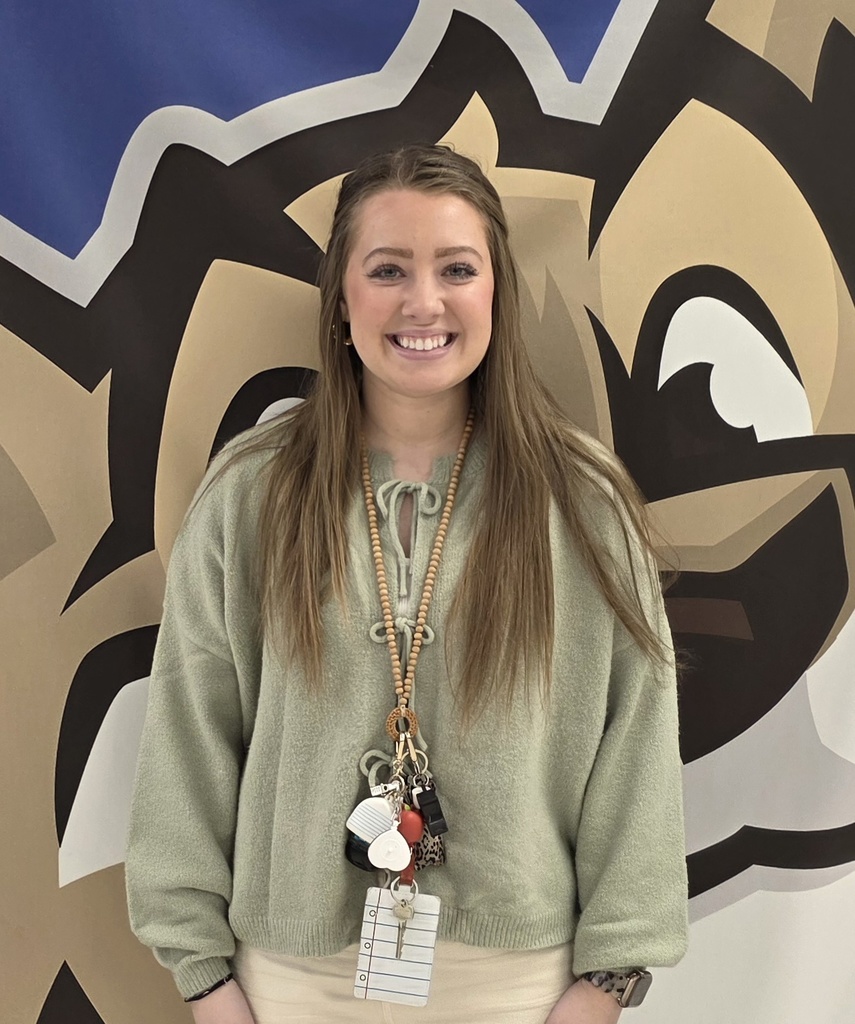 Smiling woman in green sweater with lanyard at school mural