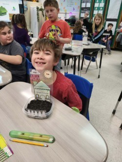 student smiling in a classroom with his model house