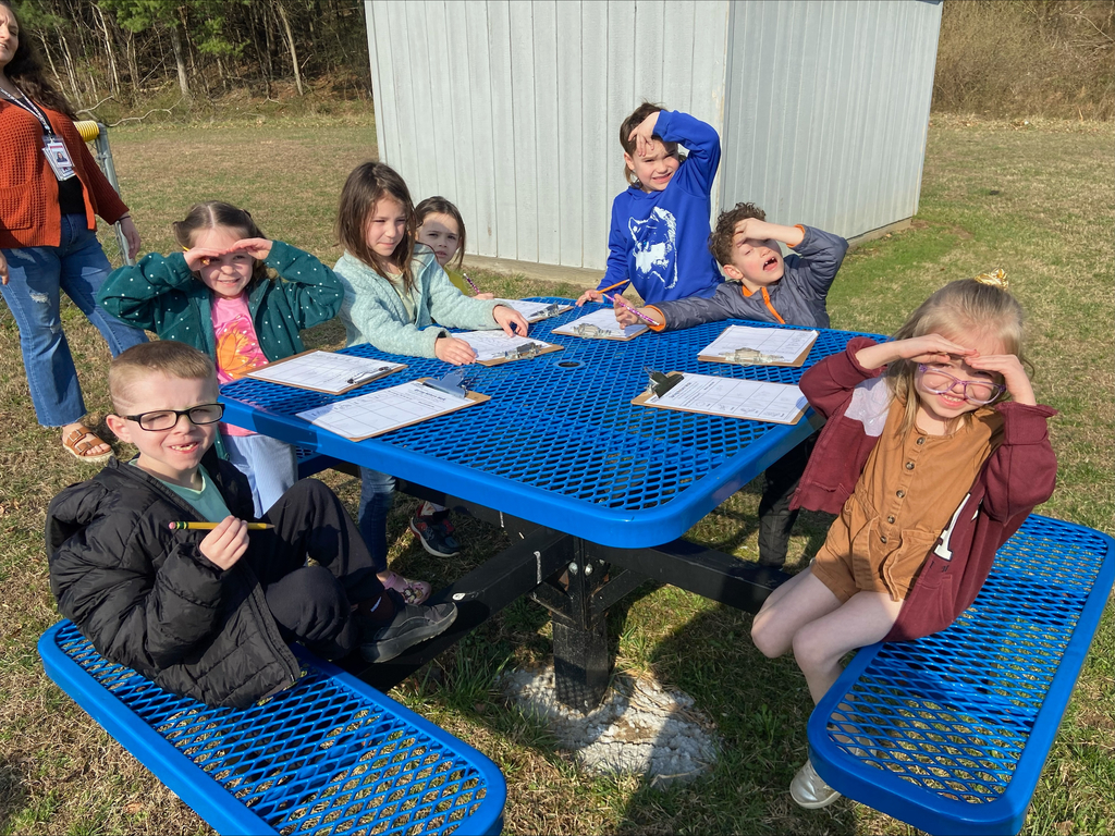 students sitting outside at a picnic table using clipboards to do school work.