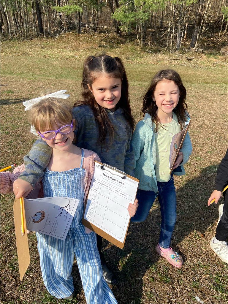 three girls in a field smiling and holding clipboards