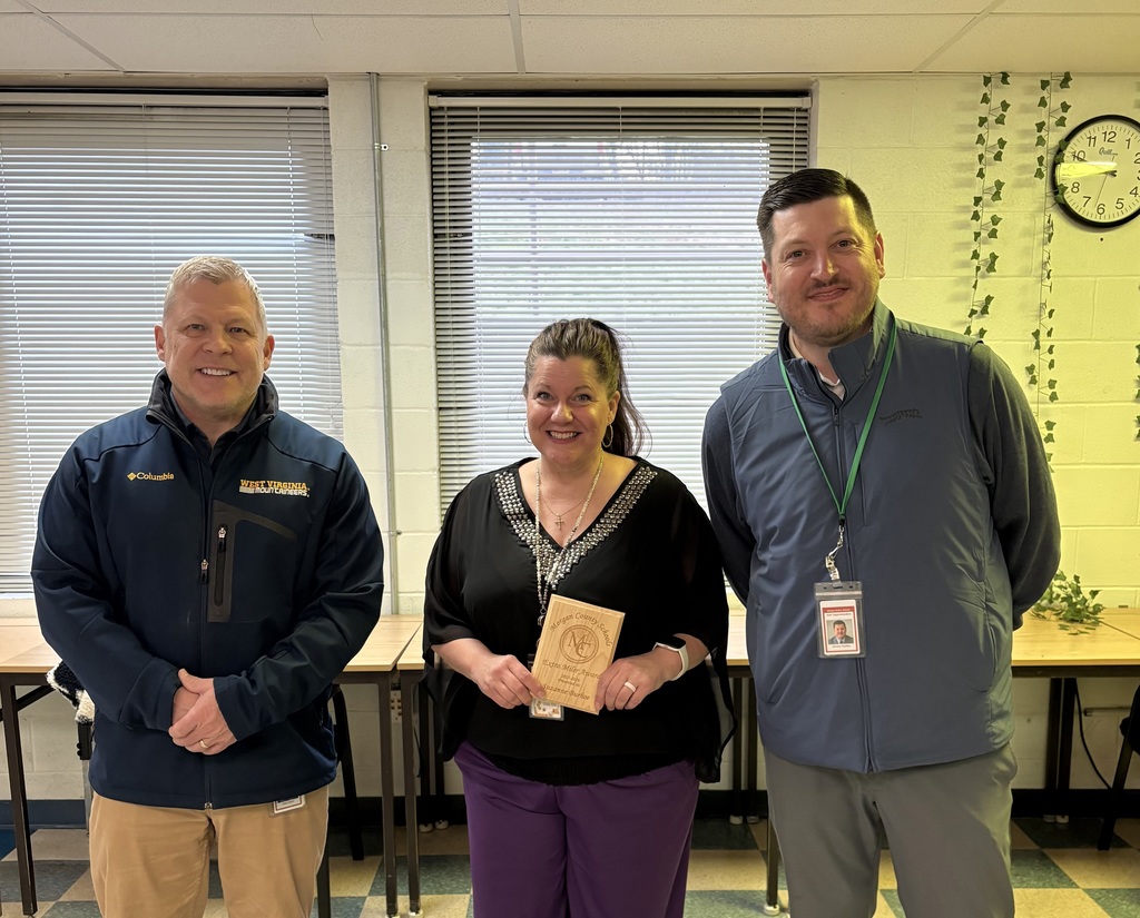Three staff members smiling, one holding an award plaque indoors.