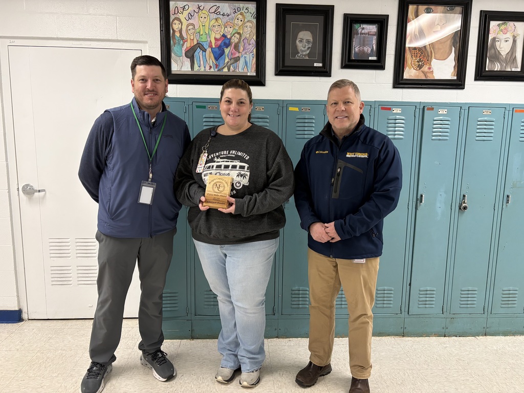 Three staff members smiling, one holding an award plaque indoors.