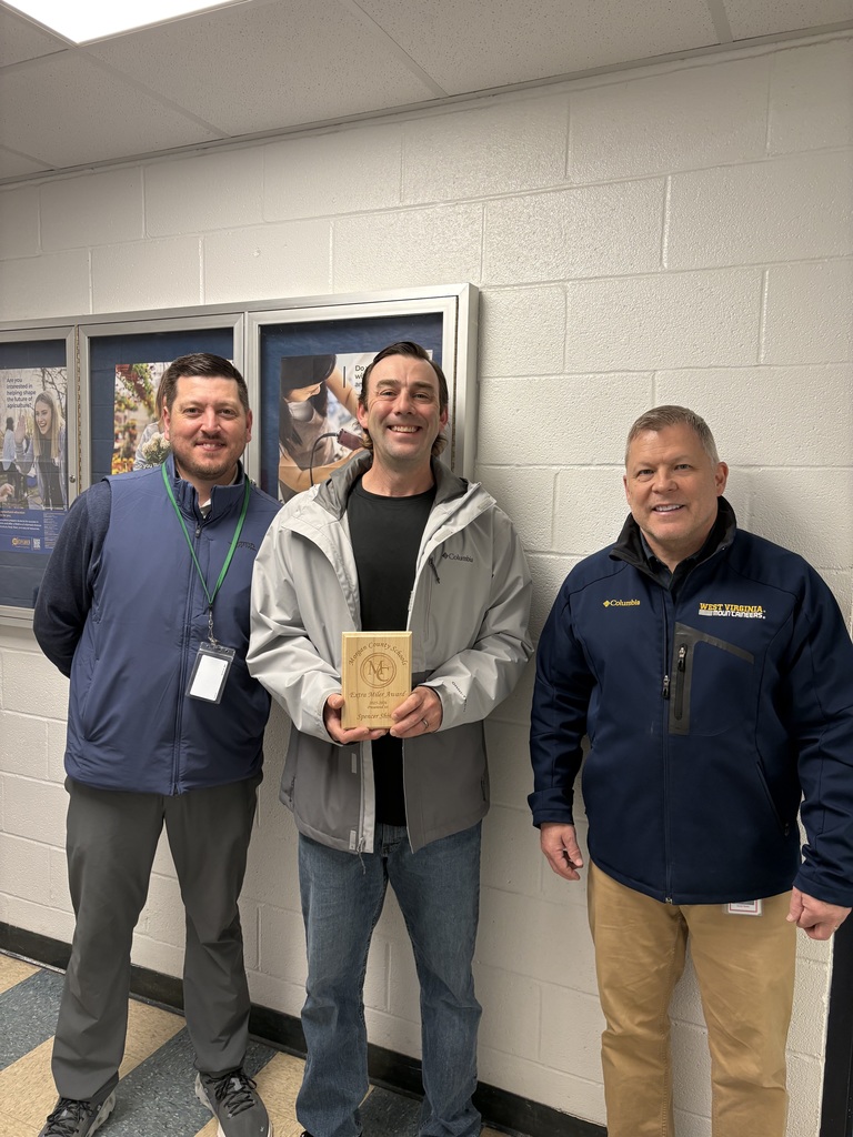 Three staff members smiling, one holding an award plaque indoors.