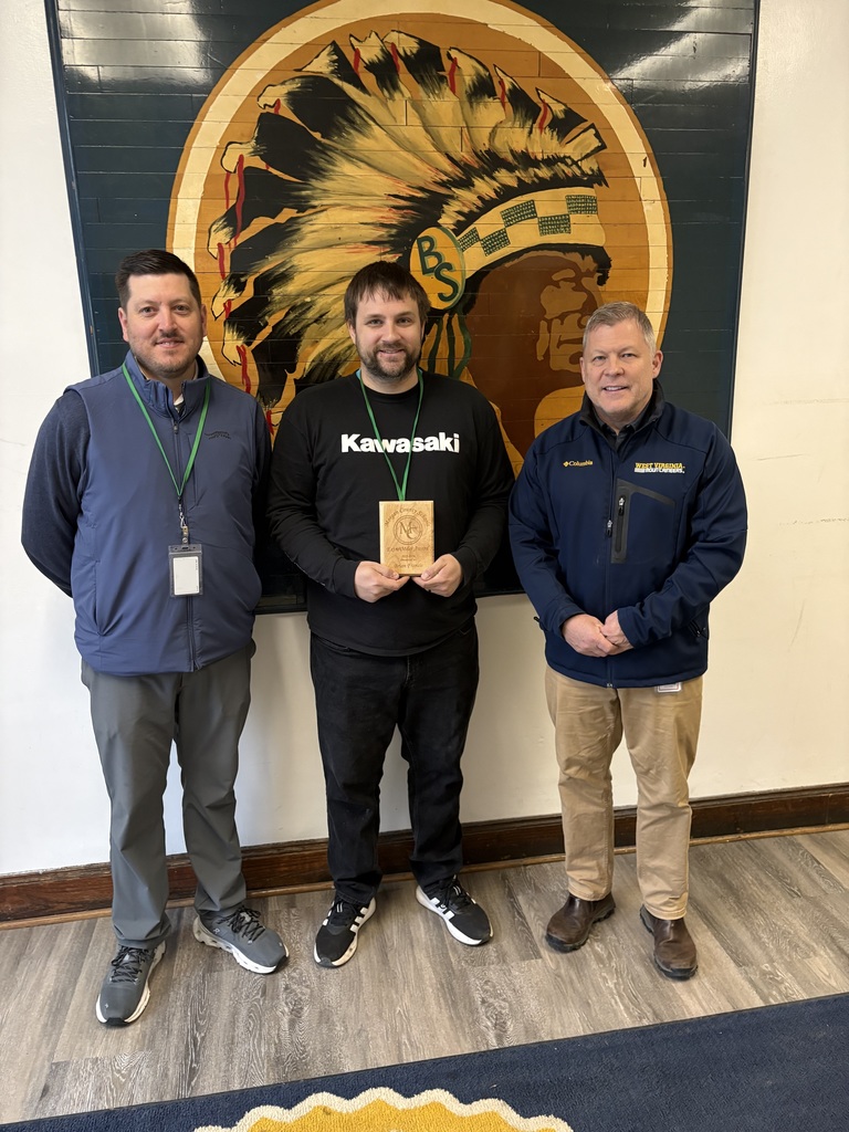 Three staff members smiling, one holding an award plaque indoors.