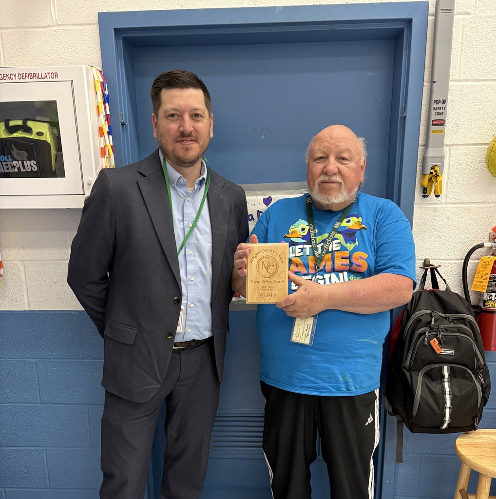 Two staff members smiling, one holding an award plaque indoors.