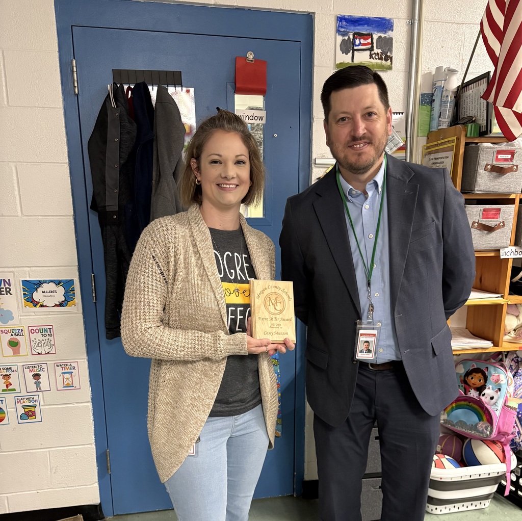 Two staff members smiling, one holding an award plaque indoors.