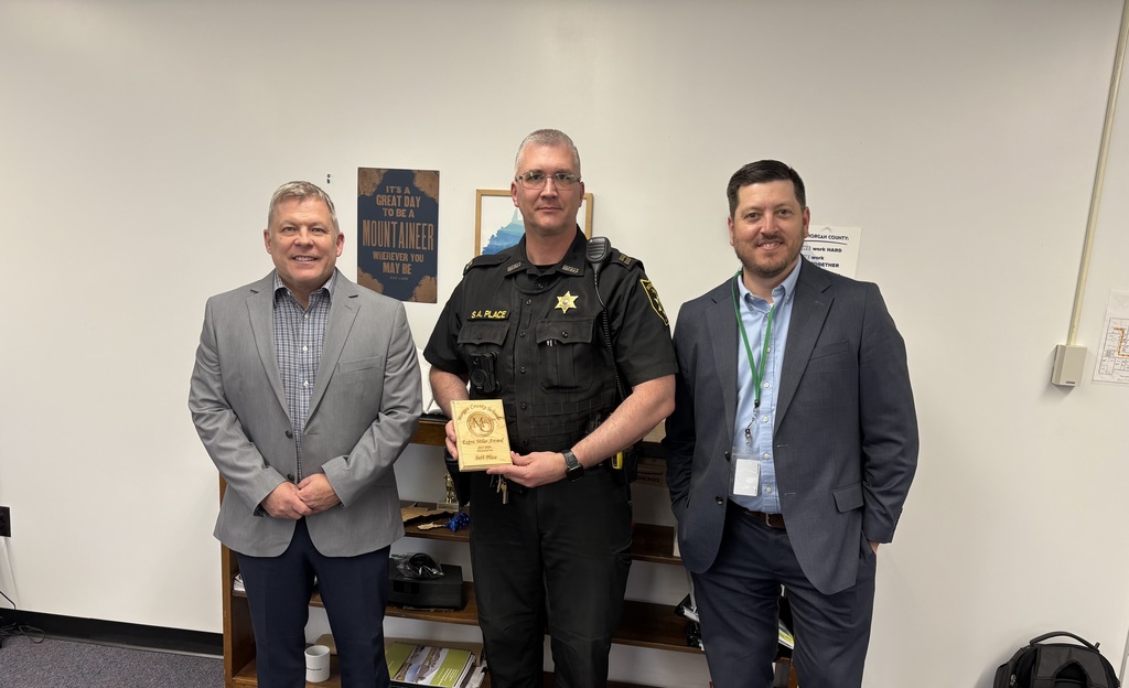 Three staff members smiling, one holding an award plaque indoors.
