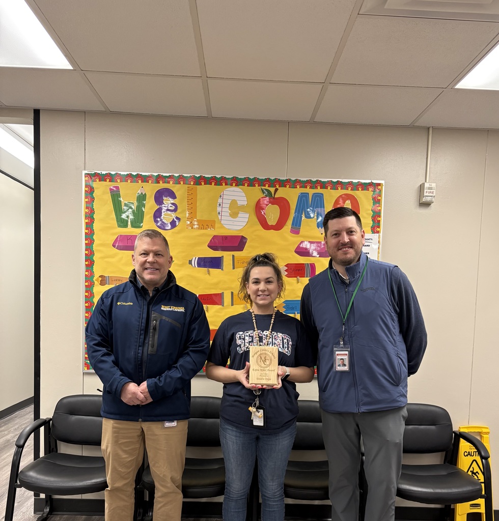 Three staff members smiling, one holding an award plaque indoors.