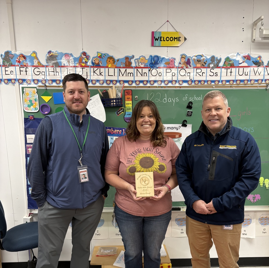 Three staff members smiling, one holding an award plaque indoors.