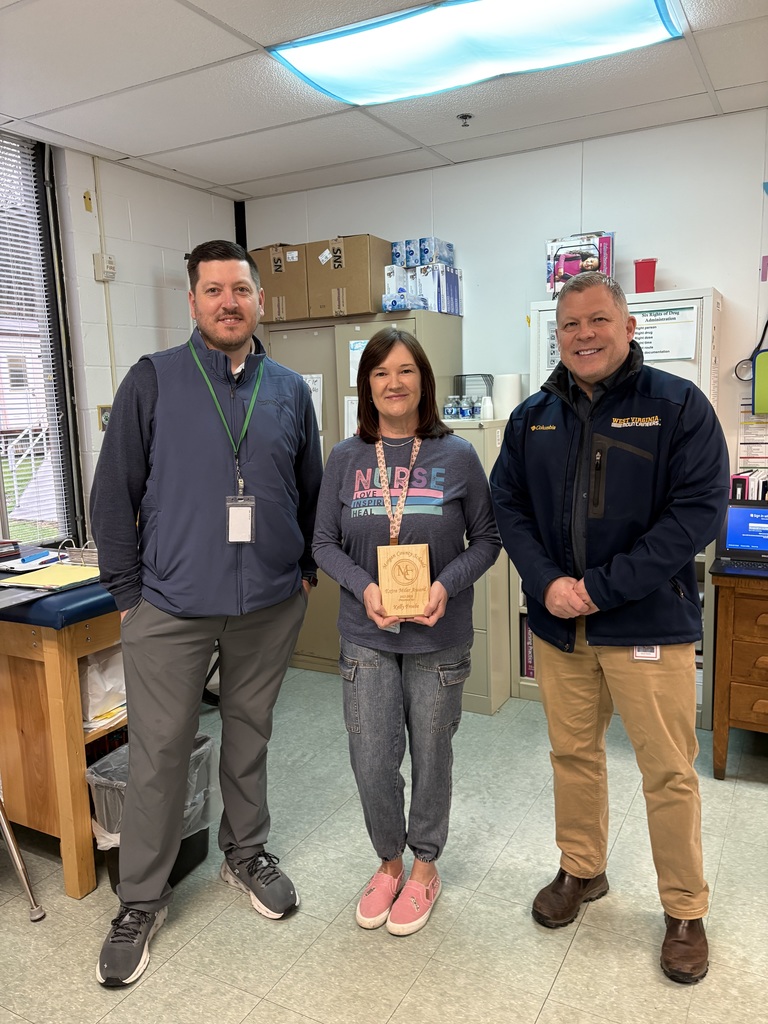 Three staff members smiling, one holding an award plaque indoors.