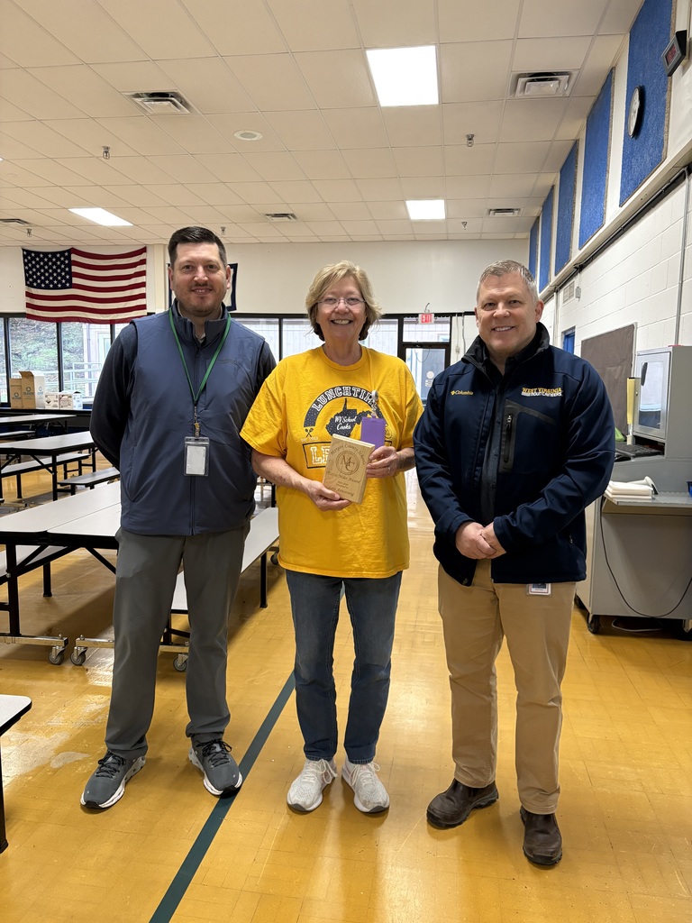 Three staff members smiling, one holding an award plaque indoors.