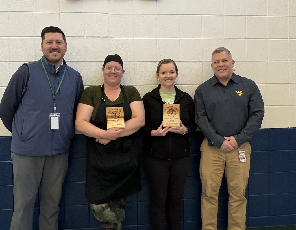 Four staff members smiling, two holding an award plaque indoors.