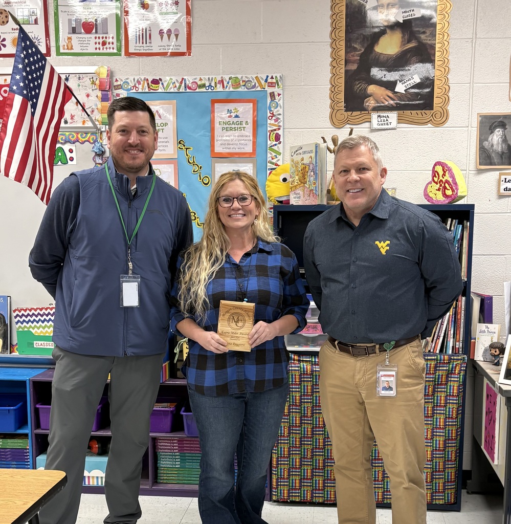 Three staff members smiling, one holding an award plaque indoors.