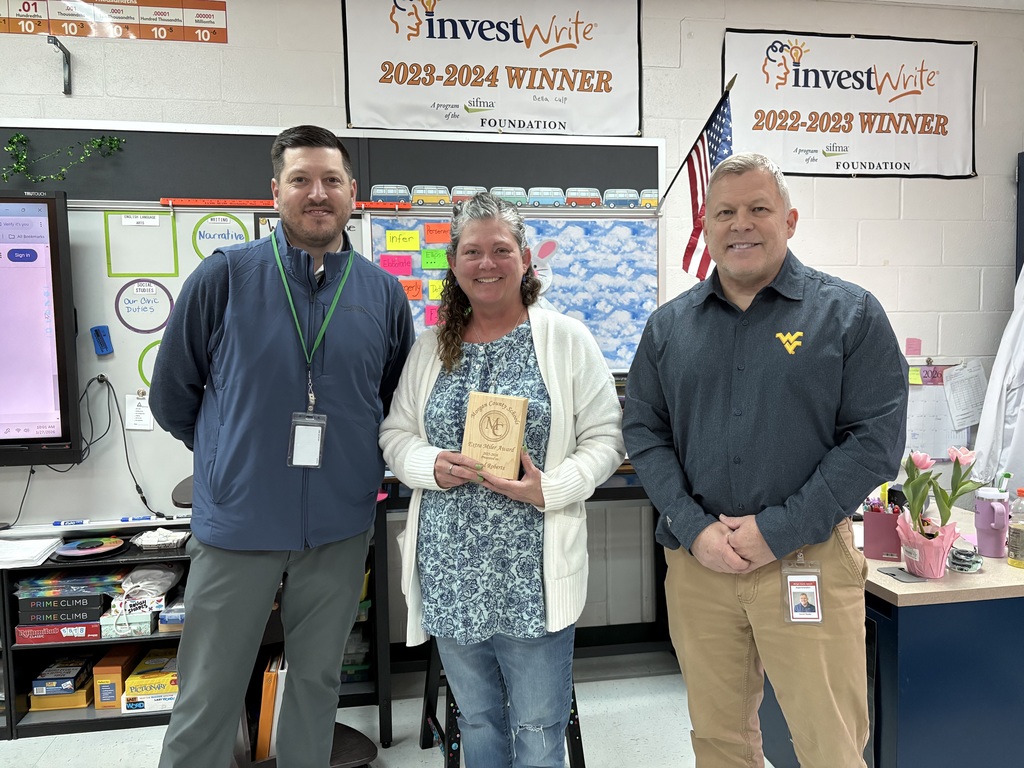 Three staff members smiling, one holding an award plaque indoors.