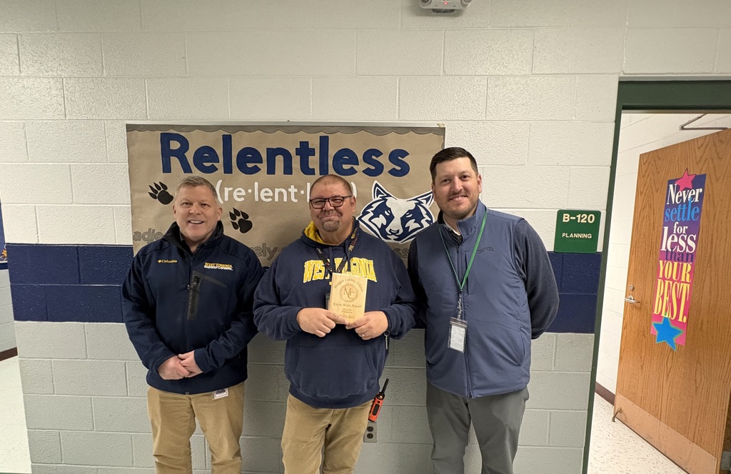 Three staff members smiling, one holding an award plaque indoors.