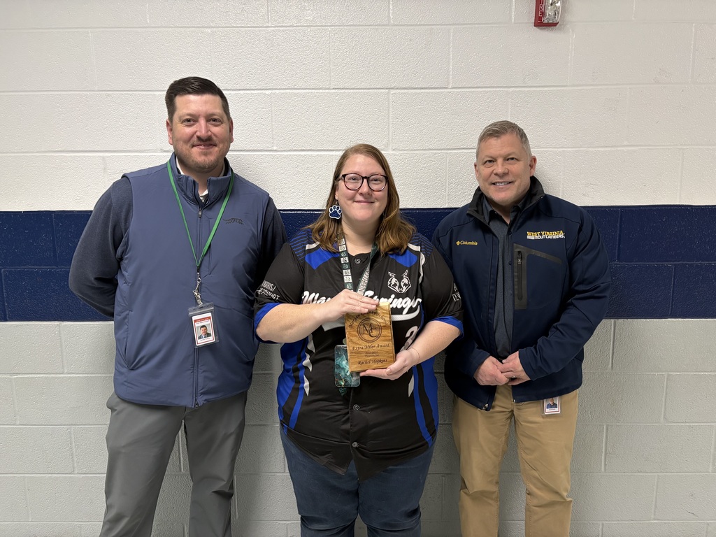 Three staff members smiling, one holding an award plaque indoors.