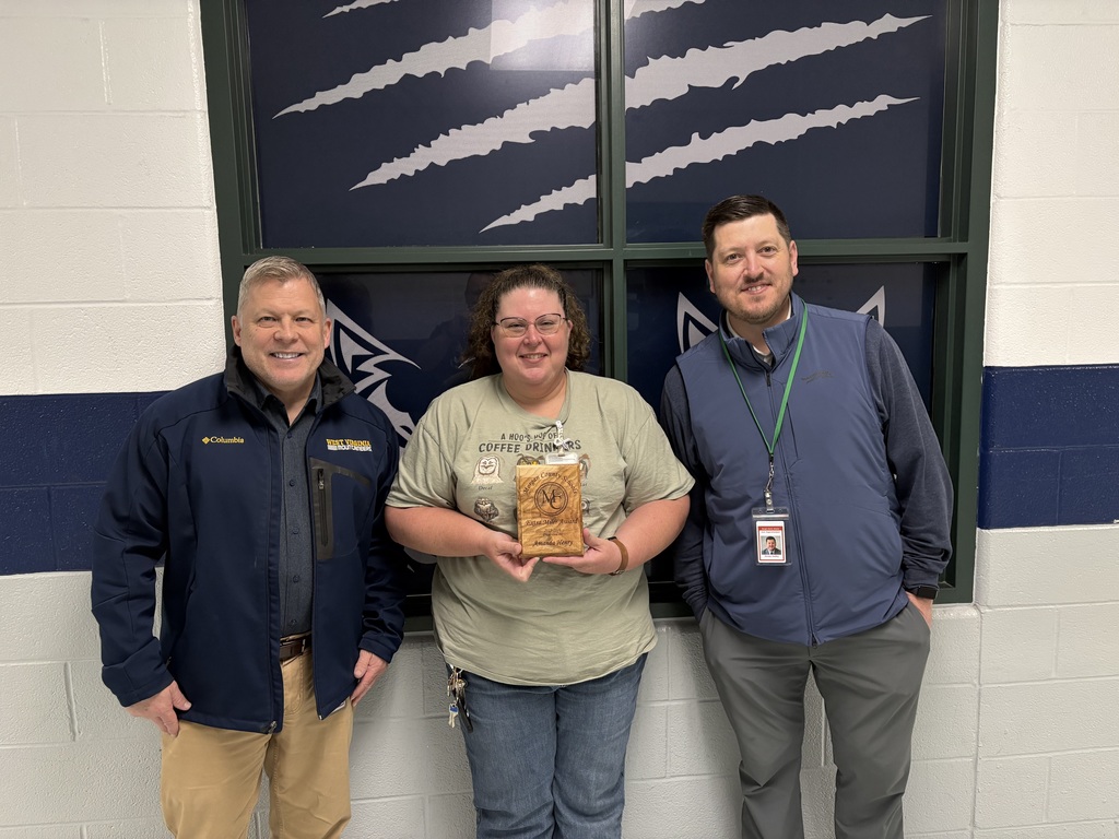 Three staff members smiling, one holding an award plaque indoors.