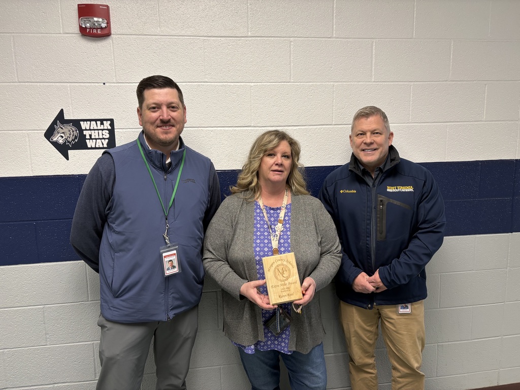 Three staff members smiling, one holding an award plaque indoors.