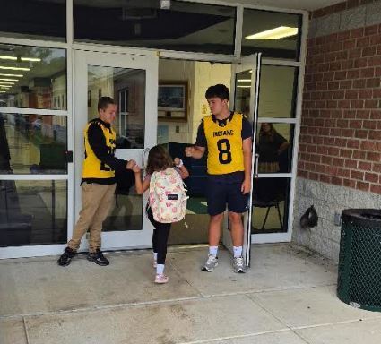 Two high school athletes greet a young scholar at the school entrance.