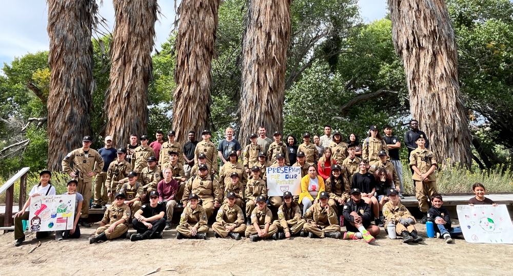 A large group of cadet corps students pose with posters alongside staff members at Big Morongo Canyon Preserve, celebrating a job well done during National Clean Up Day.