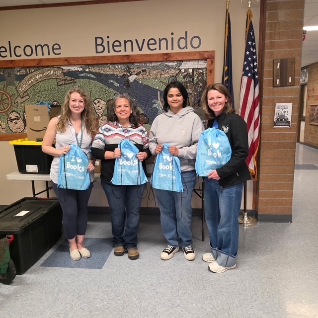 four female adults holding blue book bags