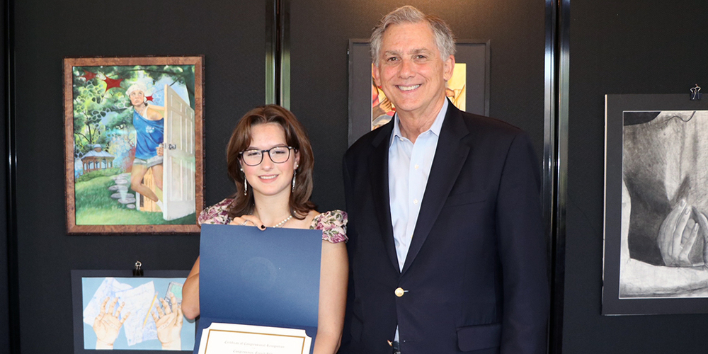 student holding award certificate in front of winning artwork and standing next to congressman