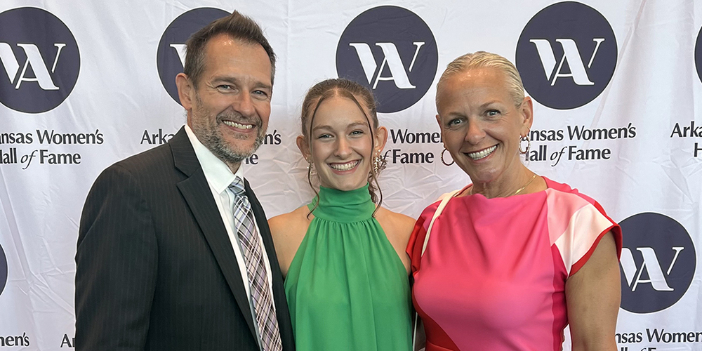 three individuals standing in front of white  backdrop with Women's Hall of Fame logo repeated across it