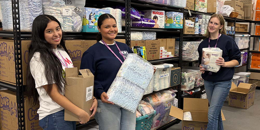 three young women holding baby supplies in front of racks full of baby supplies