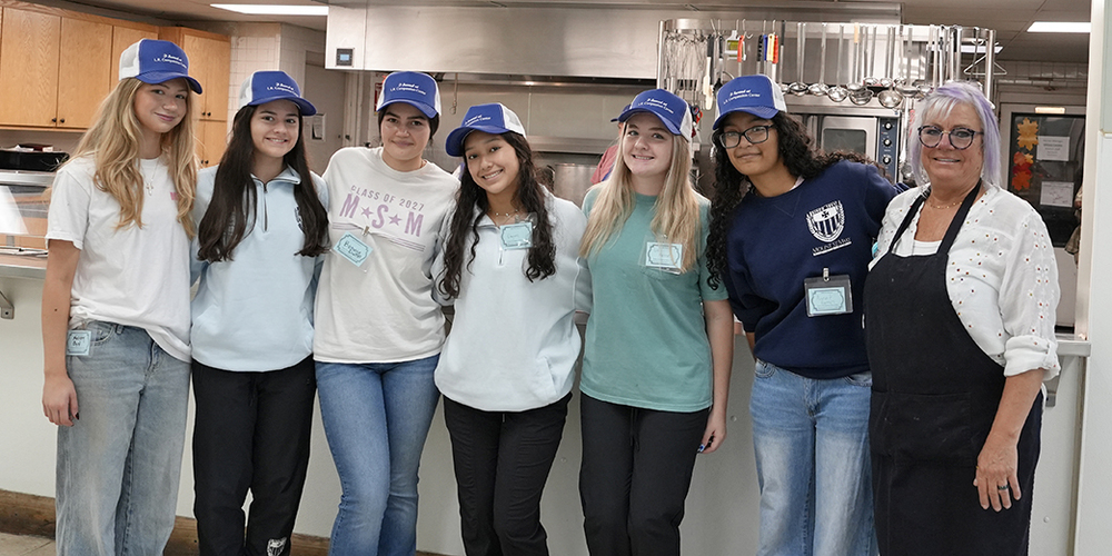 a group of young women in blue and white hats standing in front of a large commercial-size kitchen