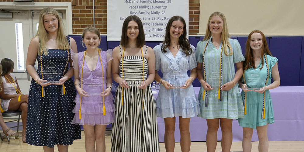 six students holding award plaques and smiling at the camera