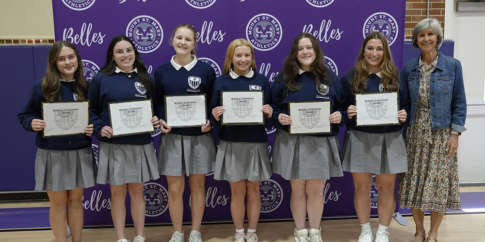 six students and an adult standing in front of a purple backdrop, holding award certificates, and smiling at the camera