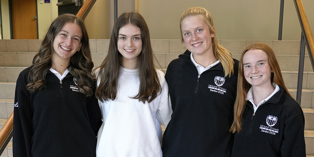 four young women standing in front of staircase in foyer and smiling at camera