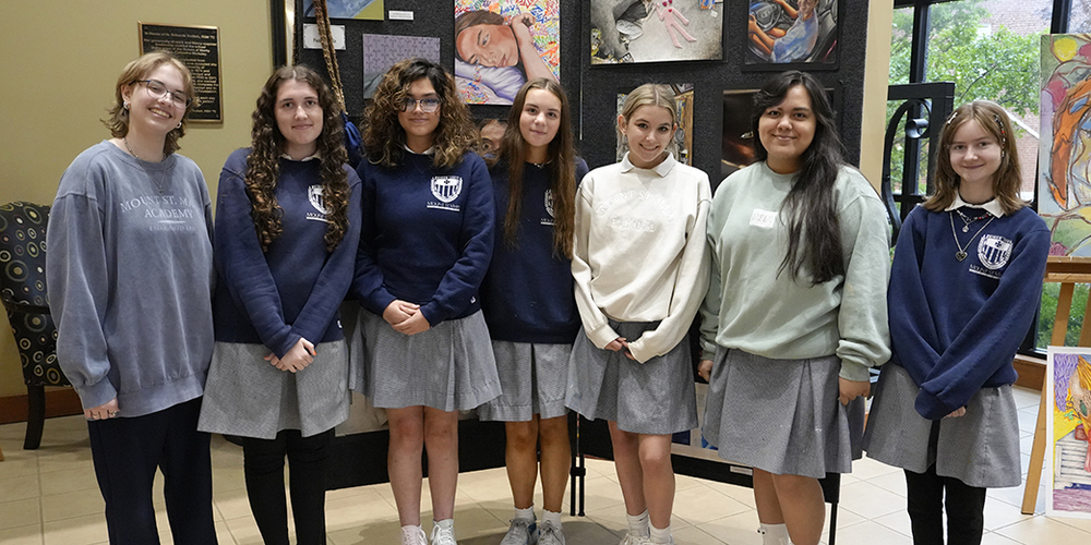 seven students standing in front of a wall displaying various pieces of artwork