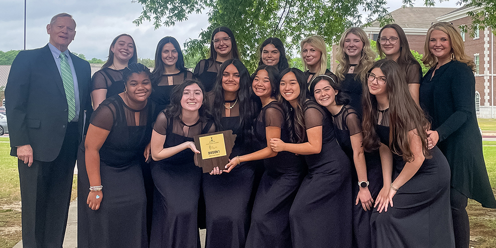 group of 14-member choir ensemble dressed in long black gowns holding award plaque