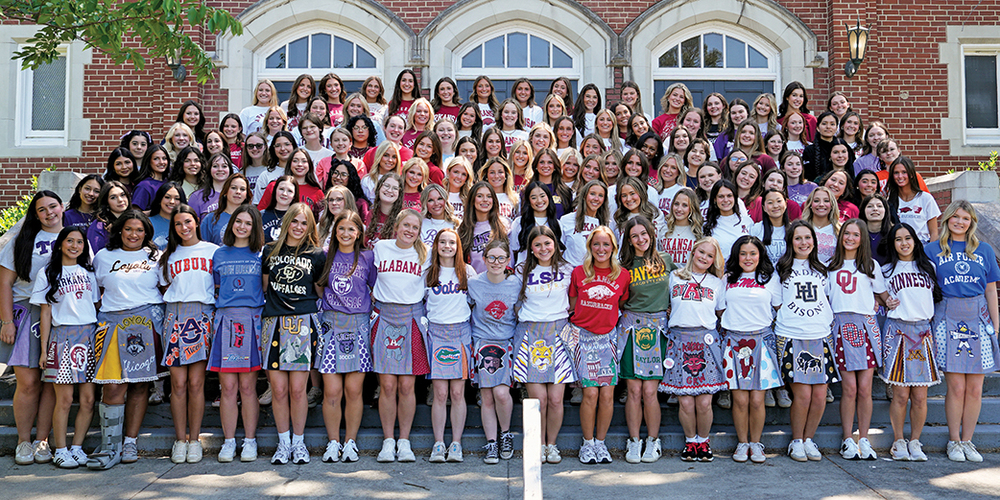 large group of students standing on steps outside of building wearing college shirts and painted uniform skirts