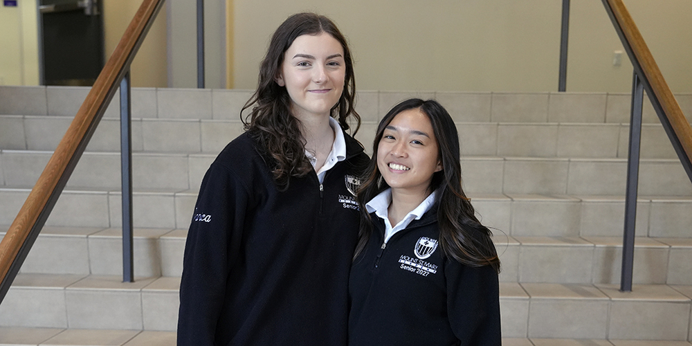 two students standing in front of staircase smiling at the camera