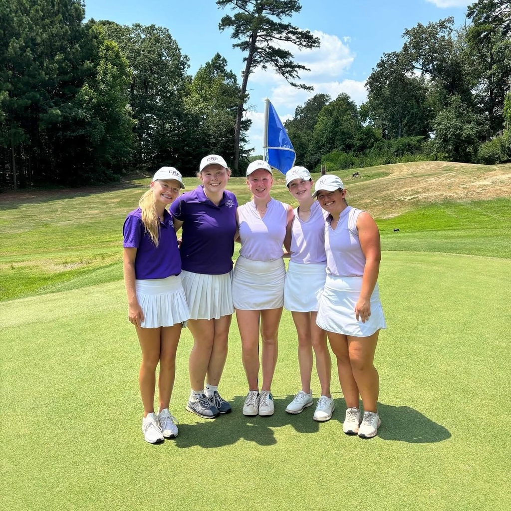 four female golfers standing on golf course in front of a hole and smiling at camera